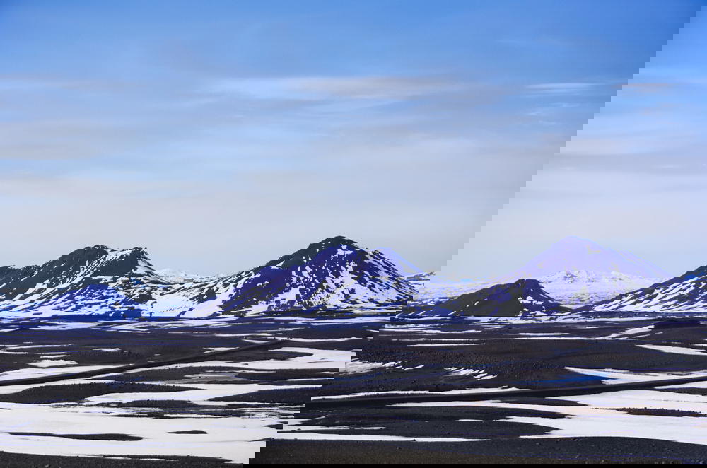 A mountain range in Iceland adorned with snow covered peaks against a backdrop of a blue sky.