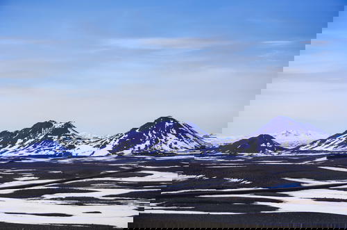 A mountain range in Iceland adorned with snow covered peaks against a backdrop of a blue sky.