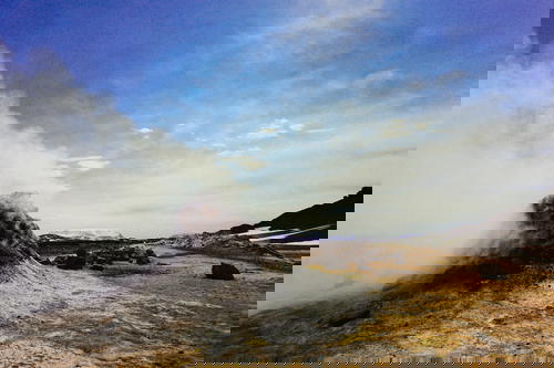 A man sitting on a sand dune next to a steaming geyser in Iceland.
