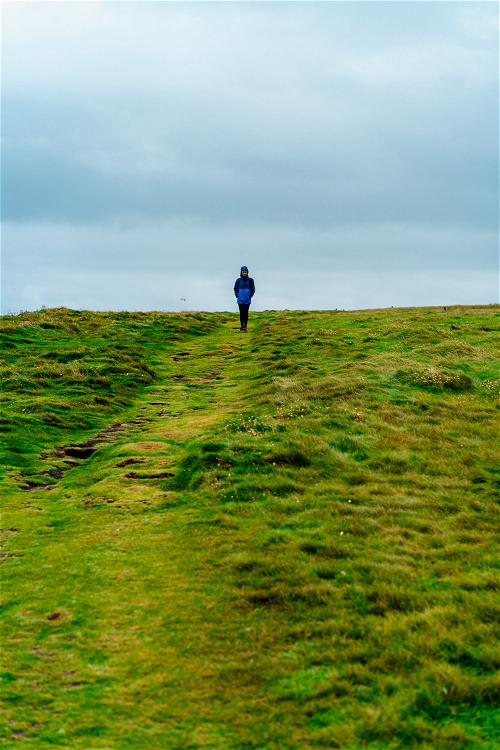 A person strolling down a grassy hill along Ireland's Wild Atlantic Way on a cloudy day.