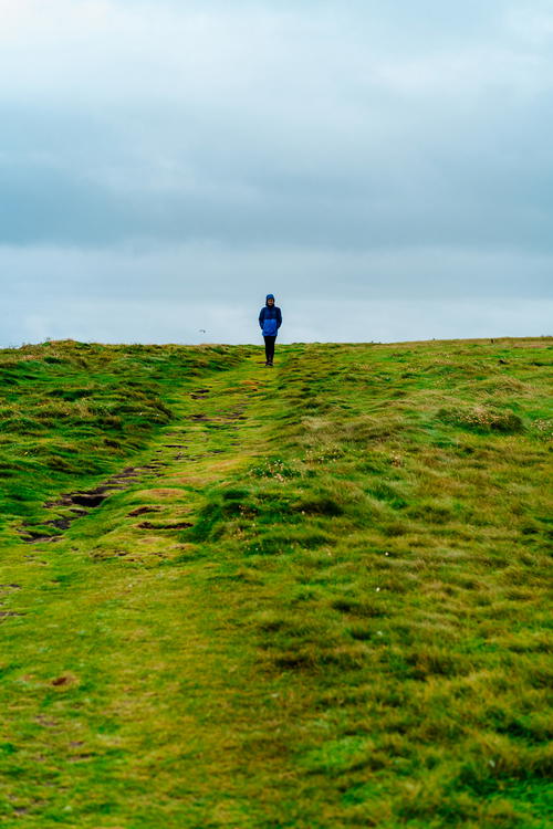 A person strolling down a grassy hill along Ireland's Wild Atlantic Way on a cloudy day.