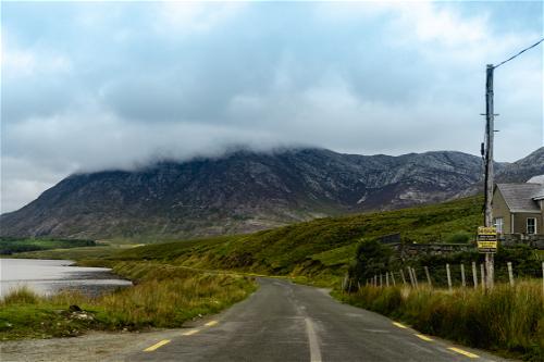 A road along the Wild Atlantic Way in Ireland leading to a lake with mountains in the background.