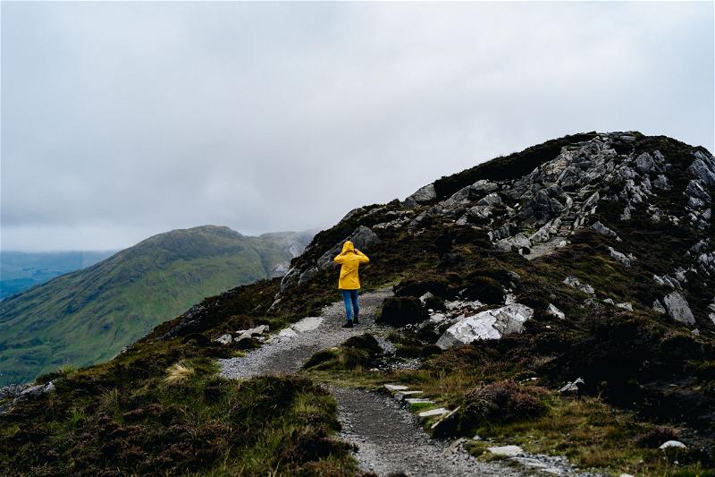 A person in a yellow raincoat standing on top of a mountain along the Wild Atlantic Way in Ireland.