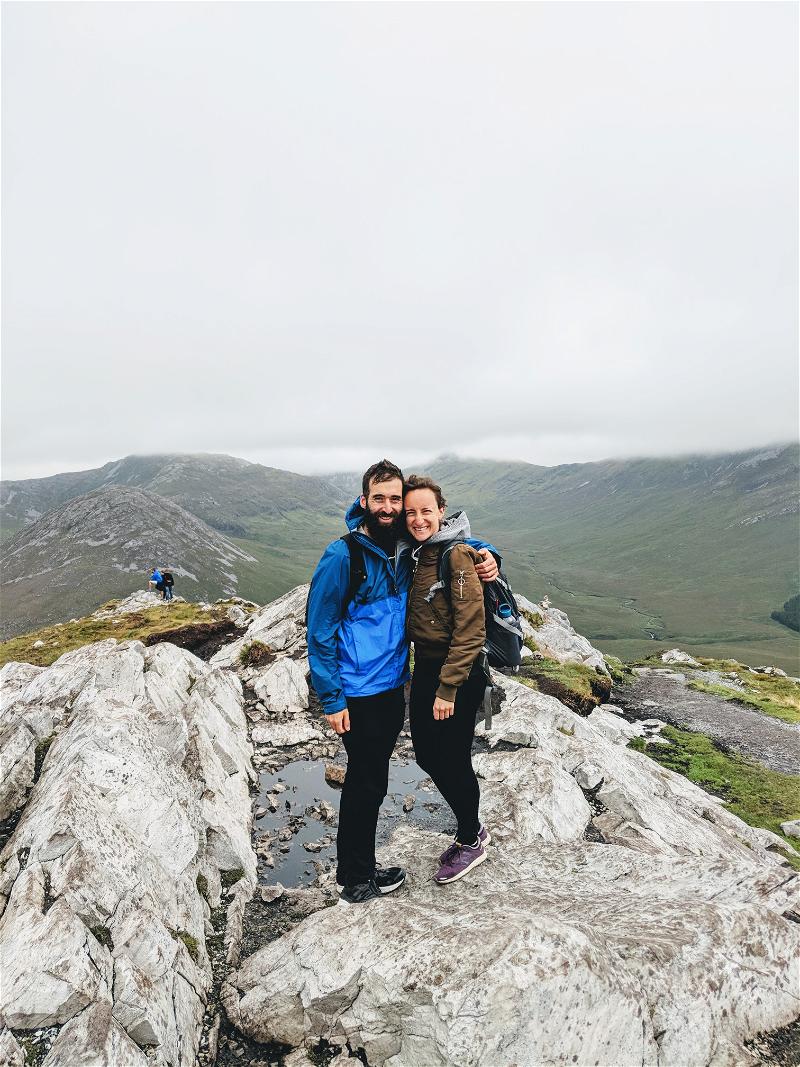 Two people atop a rocky mountain, overlooking Ireland's Wild Atlantic Way.