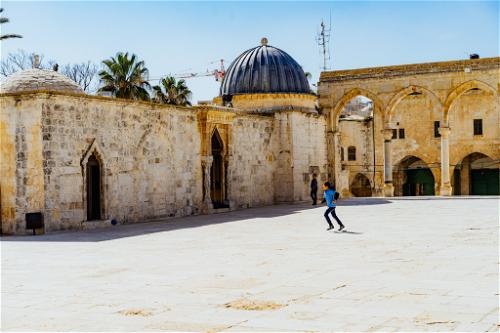 A young boy playing ball in an empty plaza at Dome of the Rock