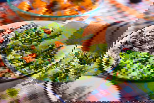 Woman using silver tongs to take cucumber salad from a big white bowl