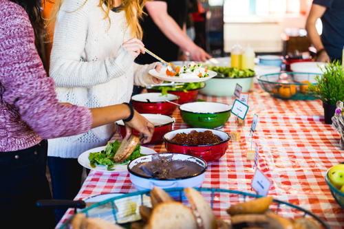 Two women taking bread and Israeli salads at a table with a red and white checked tablecloth