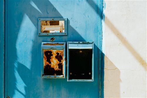 Bright blue painted door with rusted vertical mailboxes next to a white wall