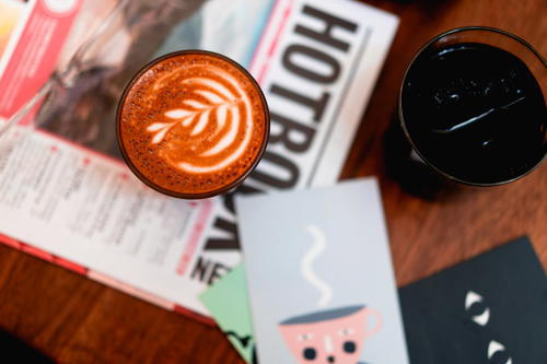 Leaf latte art in a glass cup on top of a newspaper on a wooden table at a cafe in Mexico City