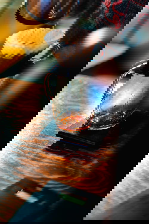 V60 pourover dripping coffee into a glass carafe on a wooden table at a coffee bar