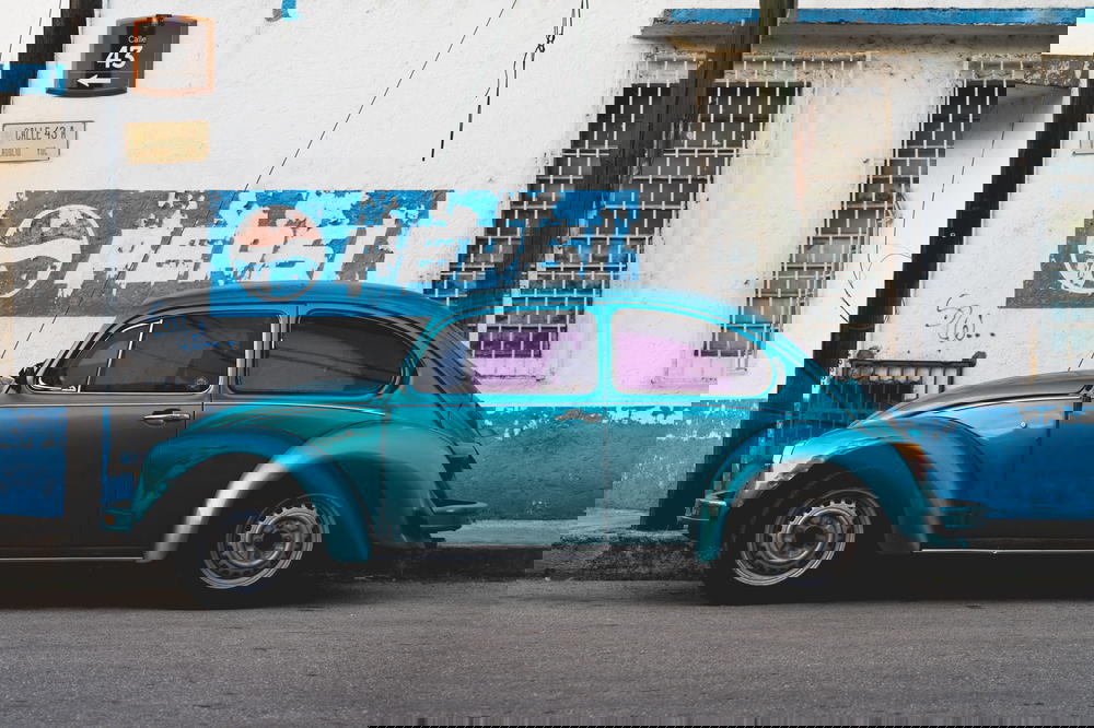 Turquoise vintage Volkswagen beetle against a whitewashed wall with a vintage PEPSI sign