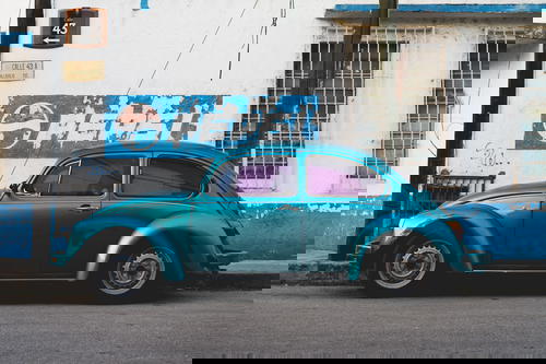 Turquoise vintage Volkswagen beetle against a whitewashed wall with a vintage PEPSI sign