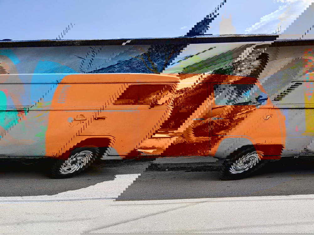 An orange van parked in front of a Mexican mural.