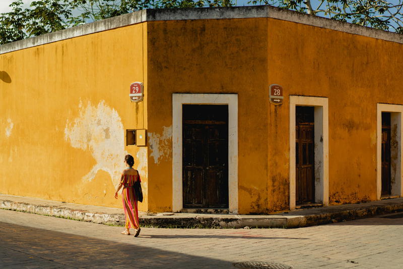A woman walking down the street in front of a yellow building in Izamal, Mexico.