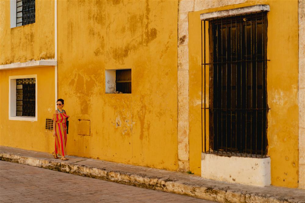 A woman standing in front of a yellow building in Izamal, Mexico.