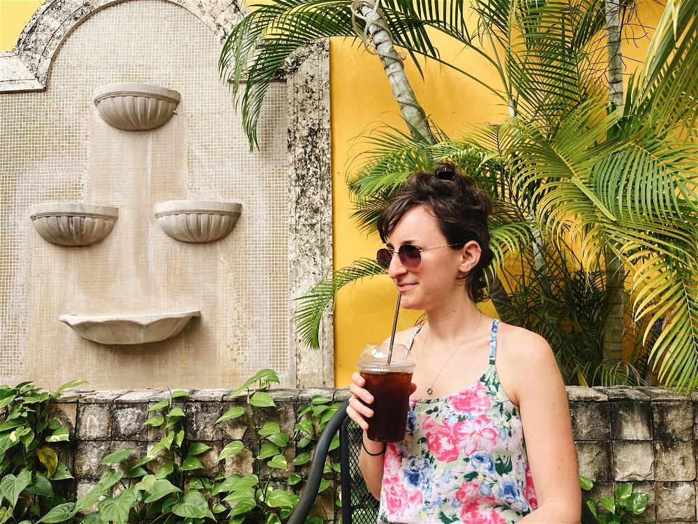 A woman drinking a drink in front of a wall.