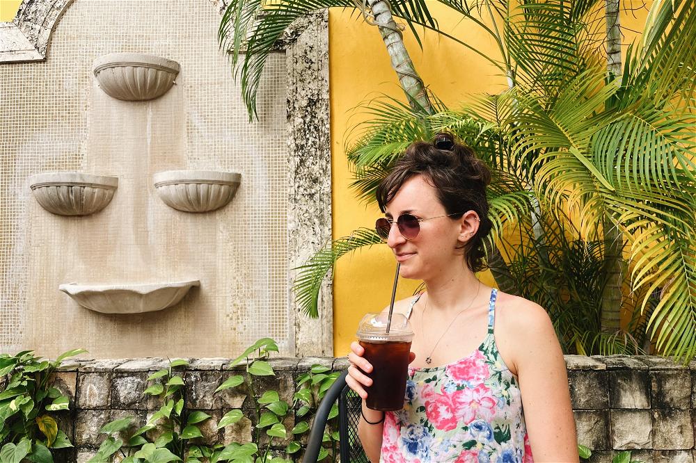 A woman drinking a drink in front of a wall.