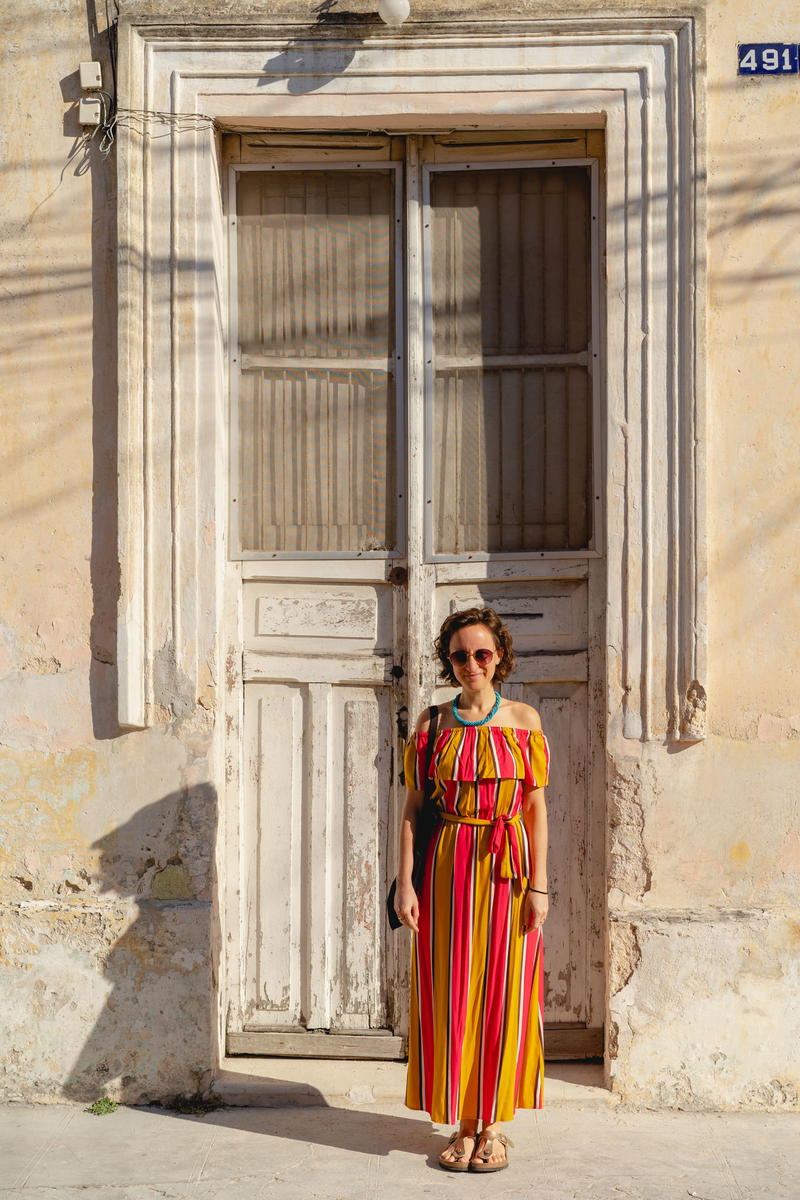 A woman in a striped dress standing in front of a door in Merida, Mexico.
