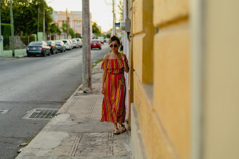 In Merida, Mexico, a woman in a striped dress leans against a wall.