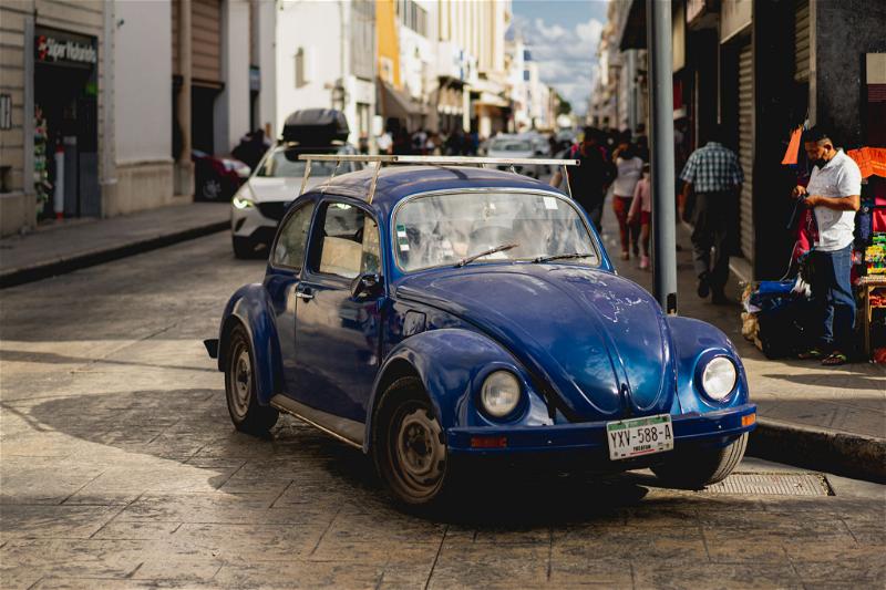 A blue Volkswagen Beetle driving down the street in Merida, Mexico.