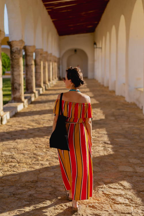A woman in a red and yellow striped dress strolling through an archway in Merida, Mexico.