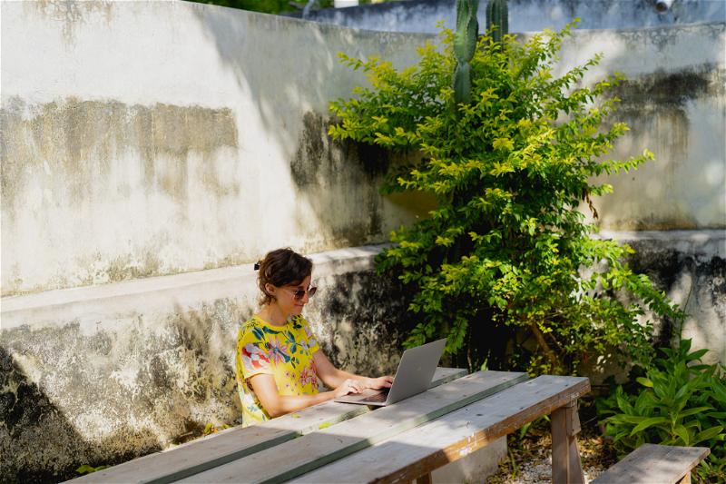 A woman sitting on a wooden bench with a laptop in Merida, Mexico.