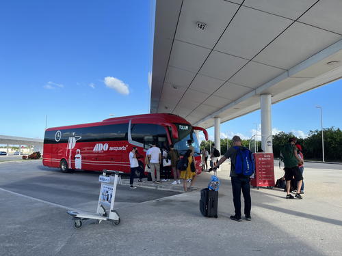 A group of people standing in front of a red bus in Merida, Mexico.