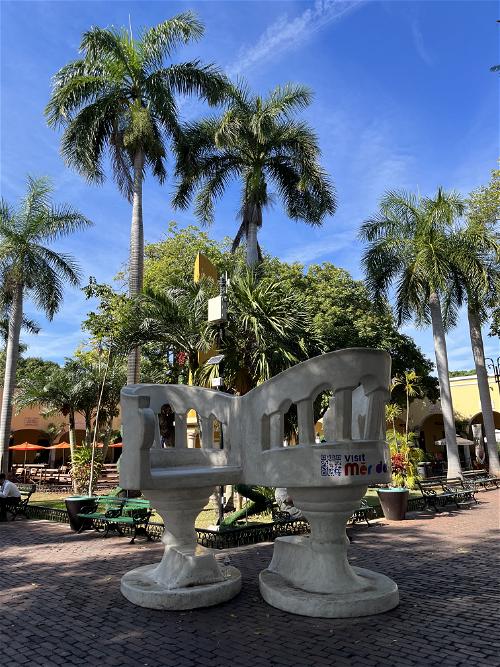 Two benches in front of palm trees in a plaza located in Merida, Mexico.