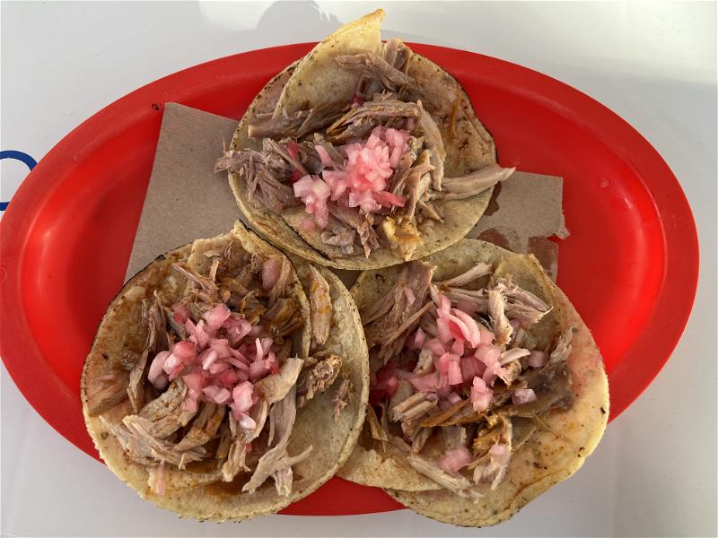 Three pork tacos on a red plate in Mexico.