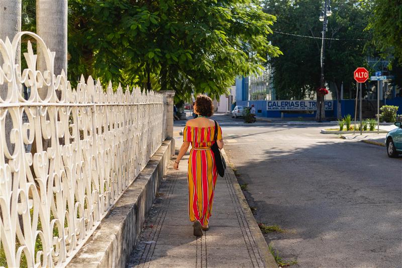 A woman in a striped dress walking down a sidewalk in Merida, Mexico.