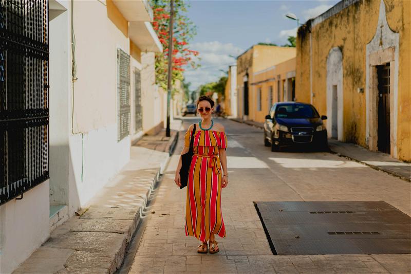 A woman in a colorful striped dress walks down a street in Merida, Mexico.