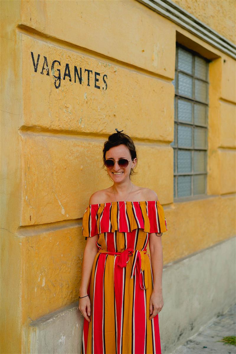 A woman in a striped off the shoulder dress leaning against a yellow wall in Merida, Mexico.