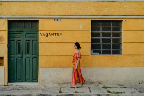 A woman in a striped dress standing in front of a yellow building in Merida, Mexico.