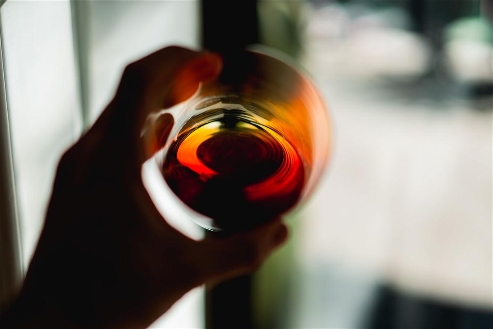 A person holding a glass of Almenegra wine in front of a window in Mexico City.