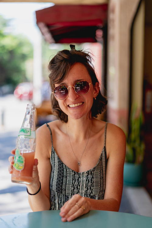 A woman from Mexico City is smiling while holding a bottle of soda.