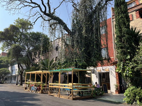 A Mexico City street with tables and chairs in front of a building.