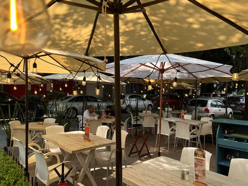 A patio with tables and chairs in Mexico City under a yellow umbrella.