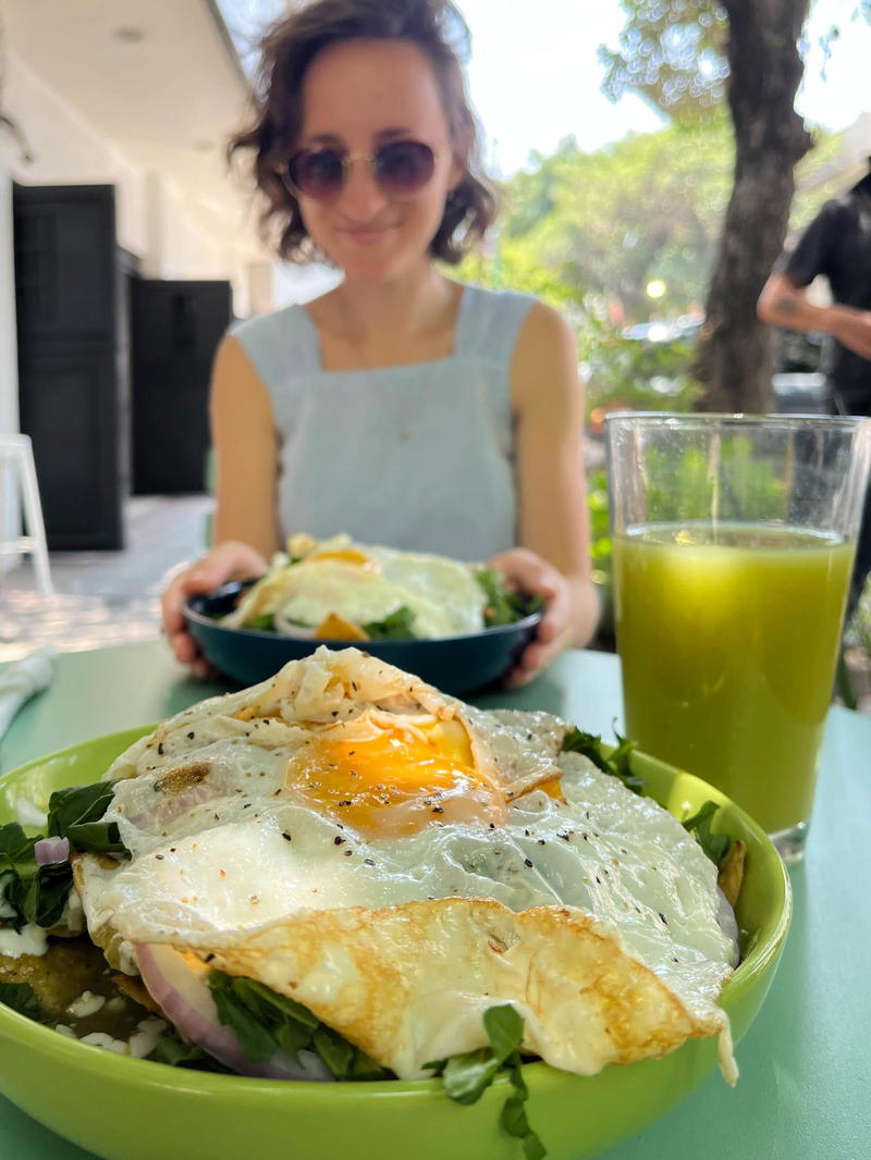 A woman is sitting at a table in Mexico City with a plate of food and a glass of juice.