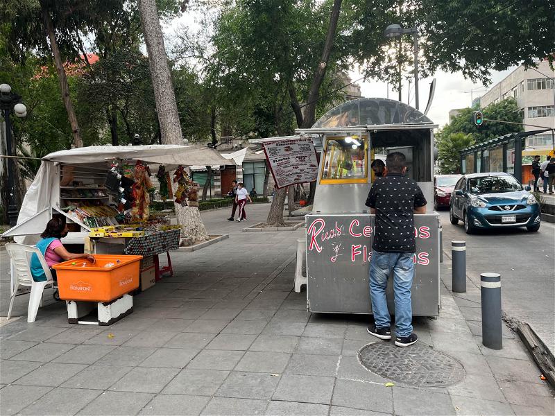 A man standing next to a food cart in Mexico City.