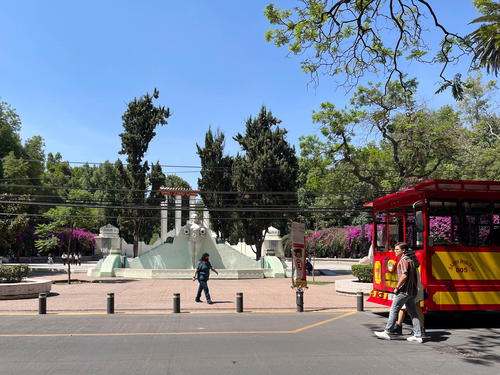 In Mexico City, a red trolley is parked in front of a fountain.