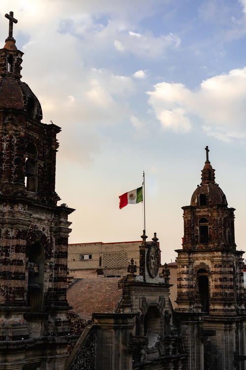 A Mexican church in Mexico City with two bell towers and a Mexican flag.