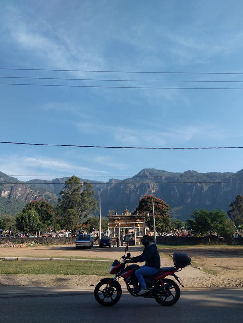 A man riding a motorcycle down a street in Mexico City with mountains in the background.
