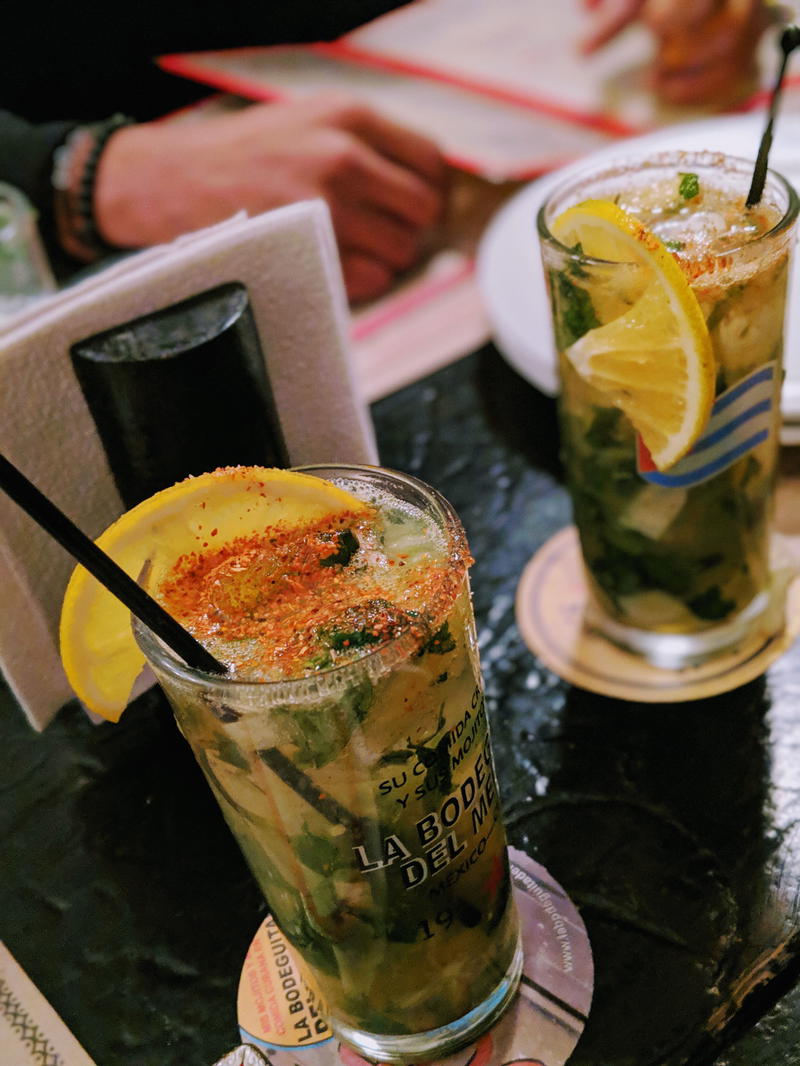 Mojito with crushed mint in a glass with a black straw and slice of lemon on a coaster