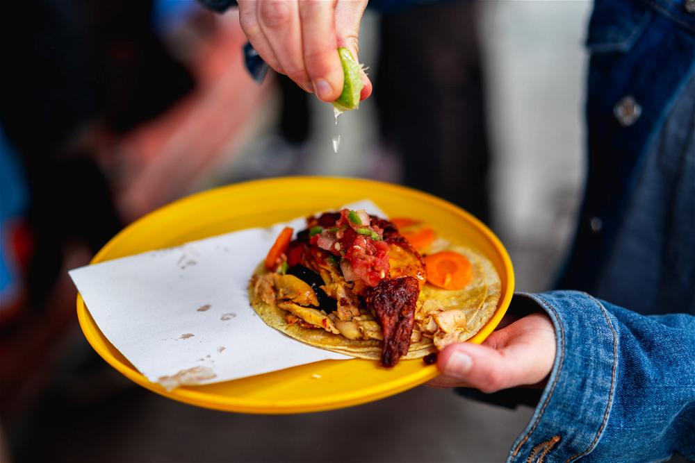 Woman squeezing a lime slice onto a rotisserie chicken taco on a yellow plate in Mexico City