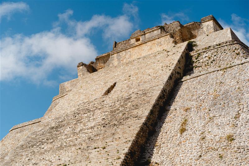 A man is standing on top of a stone tower in Uxmal, Mexico.