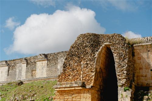 An ancient stone archway in Uxmal, Mexico framed by a picturesque cloud in the sky.