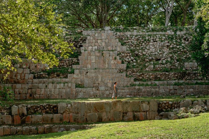 A man is standing in front of a large stone structure at Uxmal, Mexico.