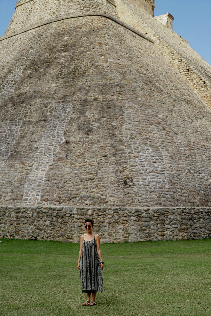 A woman standing in front of a large stone building in Uxmal, Mexico.