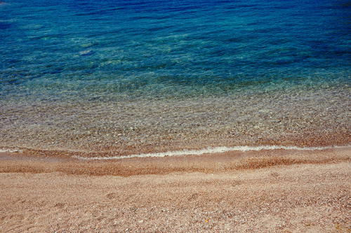 A sandy beach with blue water and a wave coming in