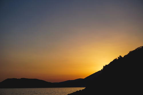 The sun is setting over the mountains and the water in Budva